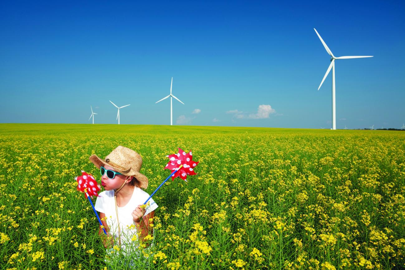 A child spinning a pinwheel in a field of flowers with wind turbines in the background