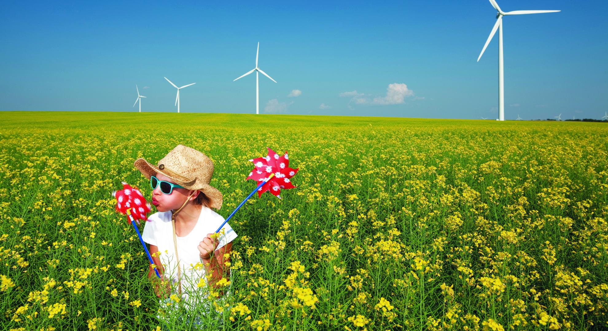 A child spinning a pinwheel in a field of flowers with wind turbines in the background