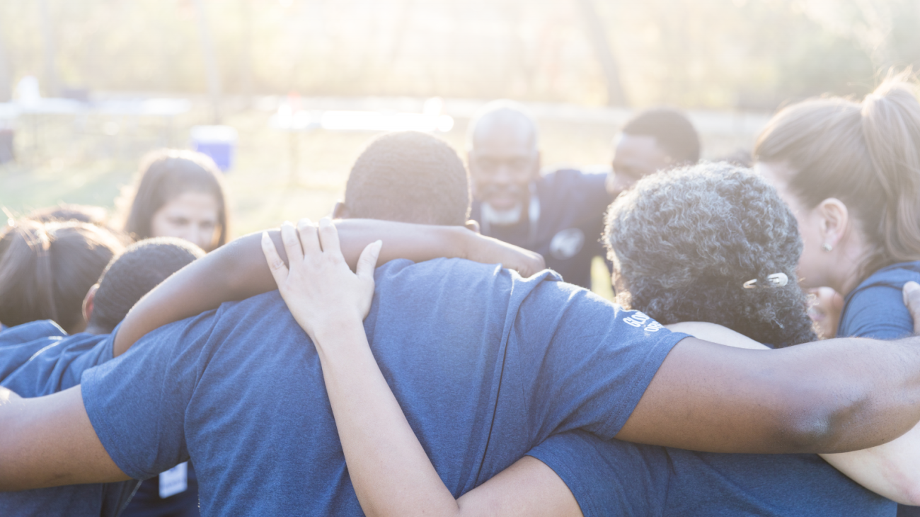 People off all ages huddling in a circle with arms around each other